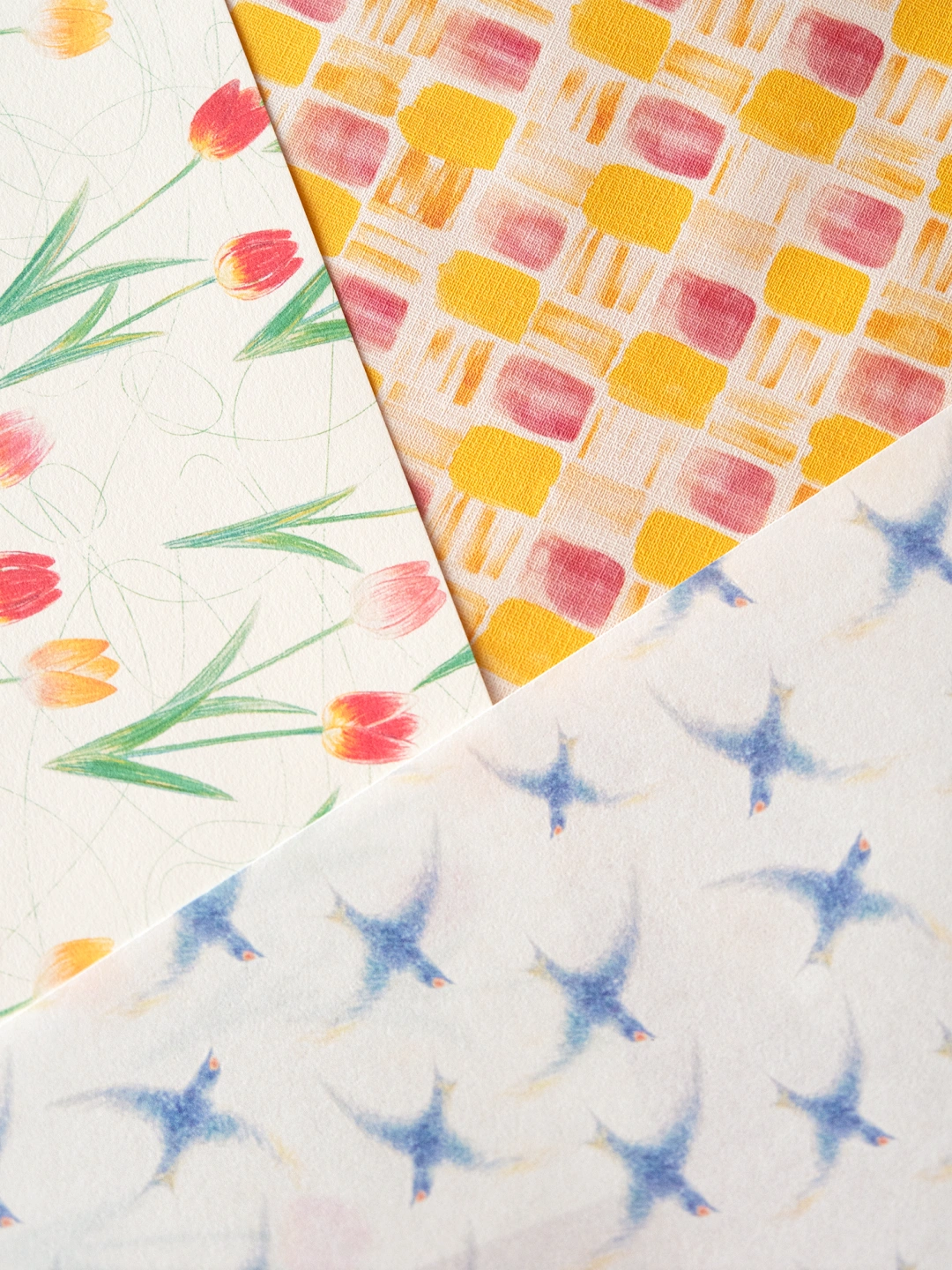 3種類のデザインペーパーを寄せて撮影した写真。 左は赤と黄とピンクのチューリップ柄、中央は黄色とピンクの四角柄、右は青いツバメ柄。