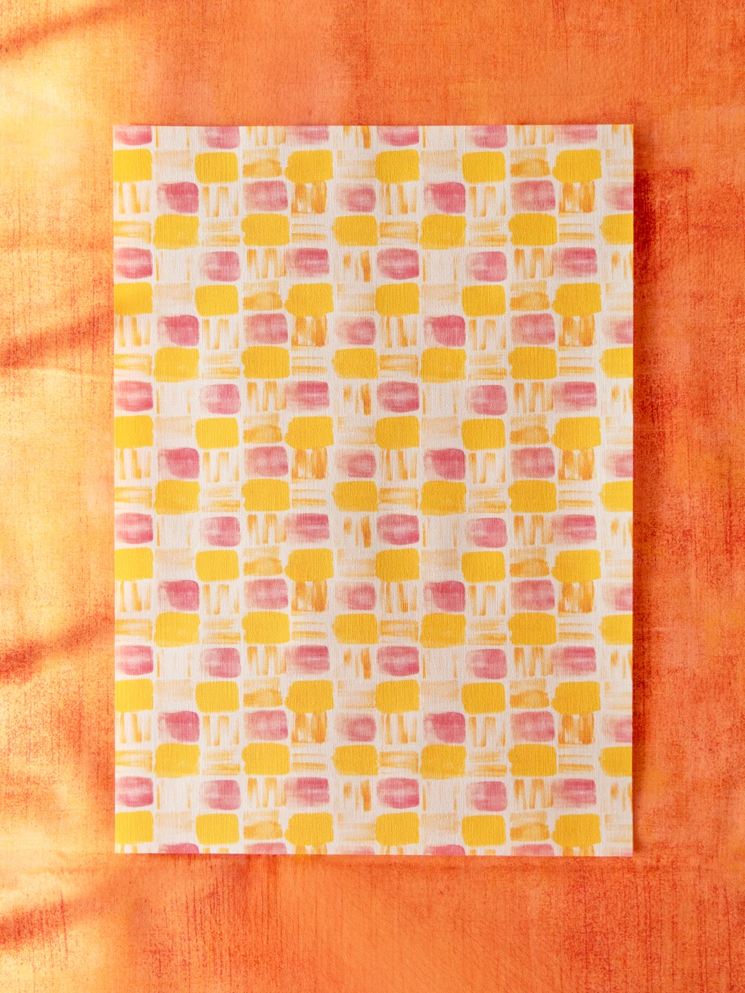 オレンジ色の布の上に置かれたデザインペーパー。黄色とピンクの四角柄。