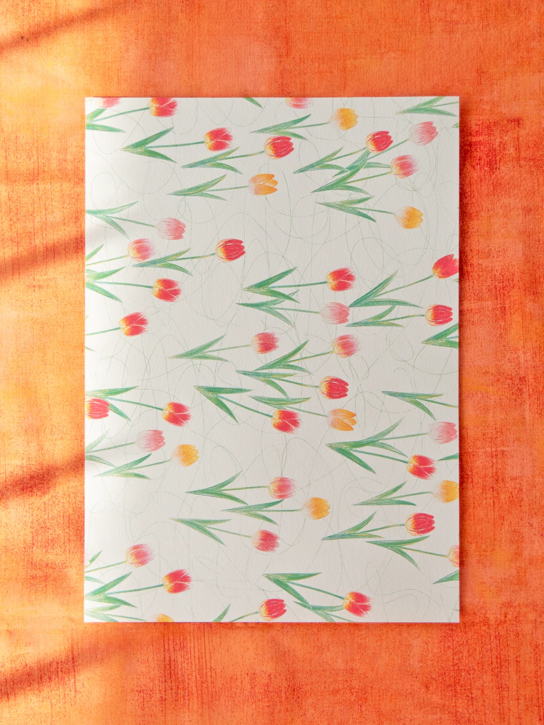 オレンジ色の布の上に置かれたデザインペーパー。赤・黄・ピンクのチューリップ柄。